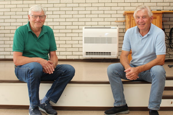 to menn sitter foran en varmepumpe, inne i menighetshuset